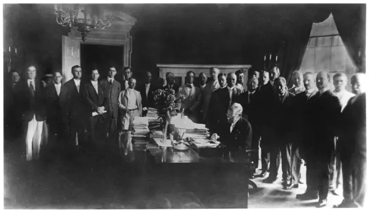 President Wilson signing legislation at his desk, surrounded by officials